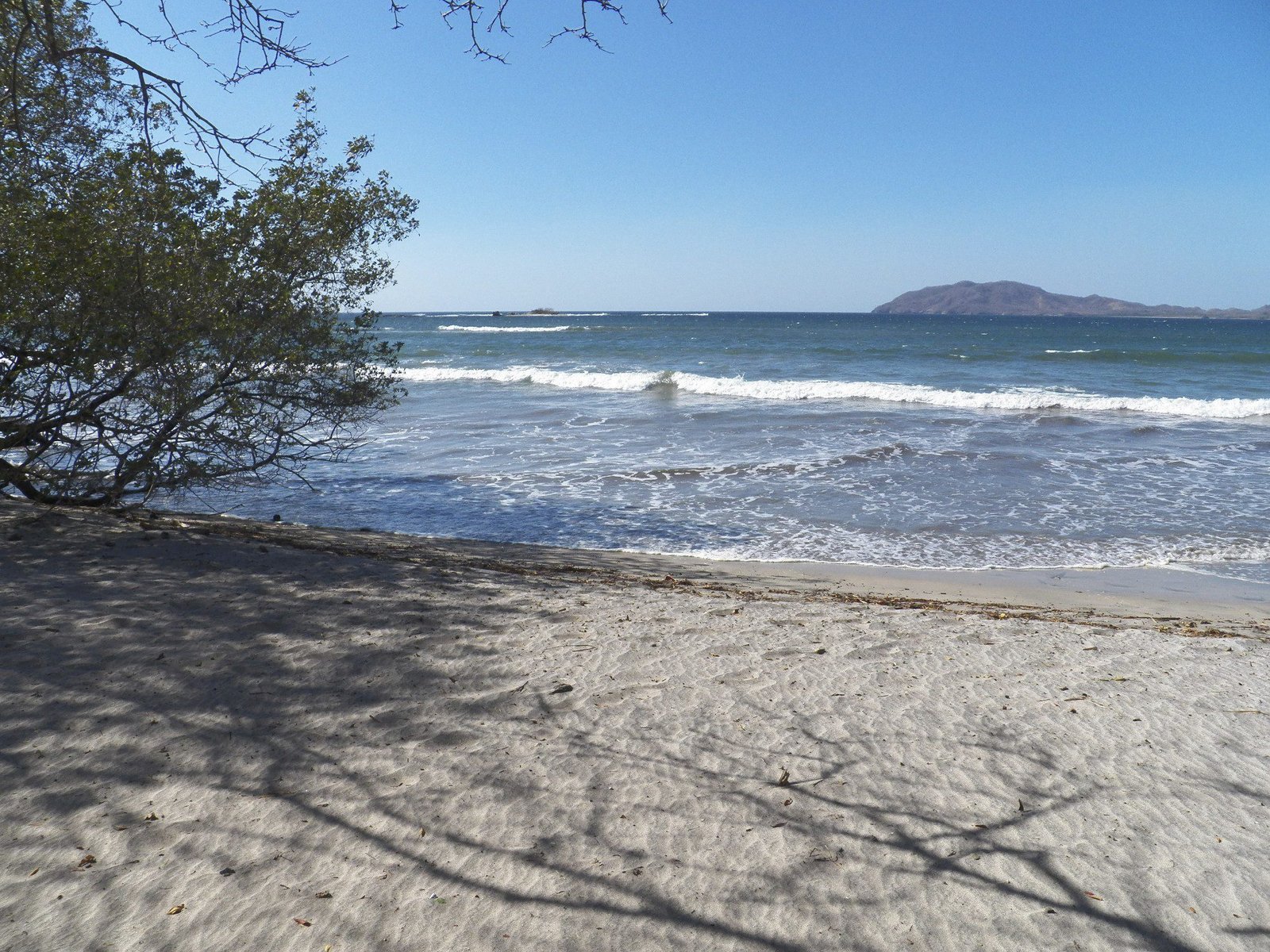 Wit strand met zee en berg op achtergrond.