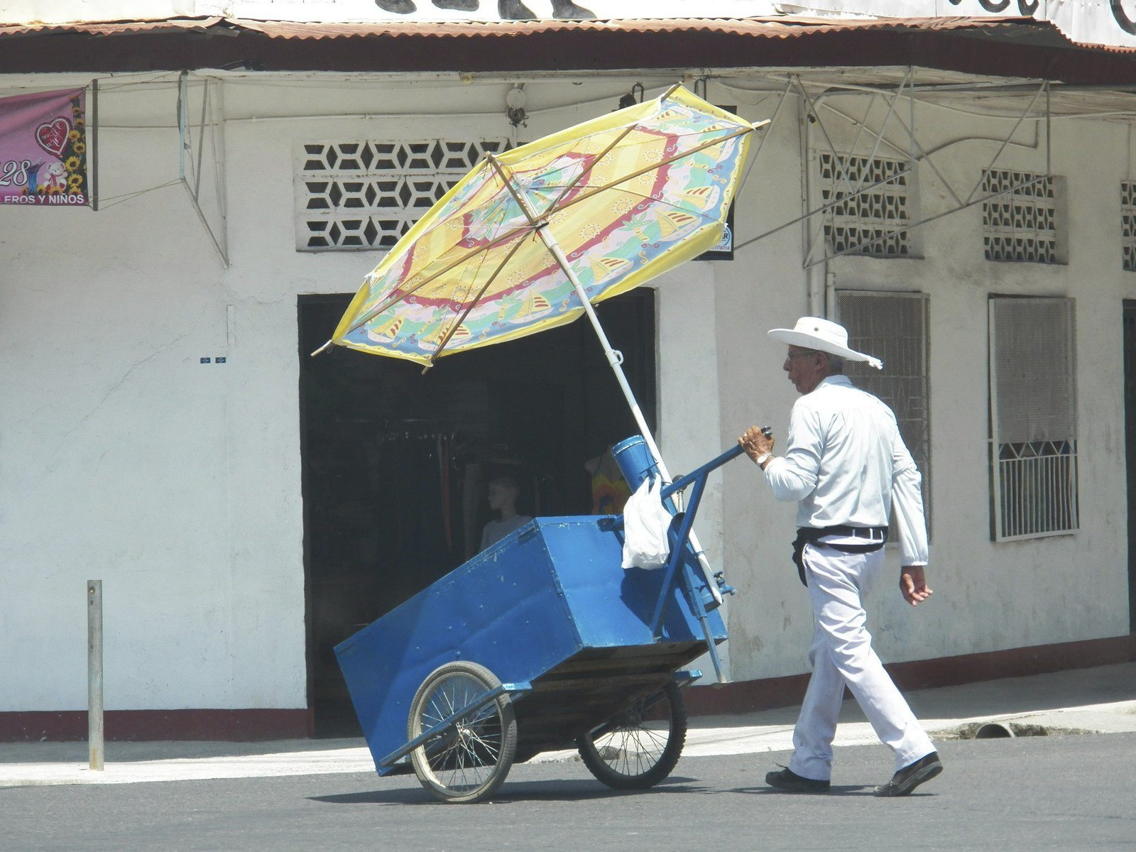Man in het wit met blauwe stootkar en gele parasol.