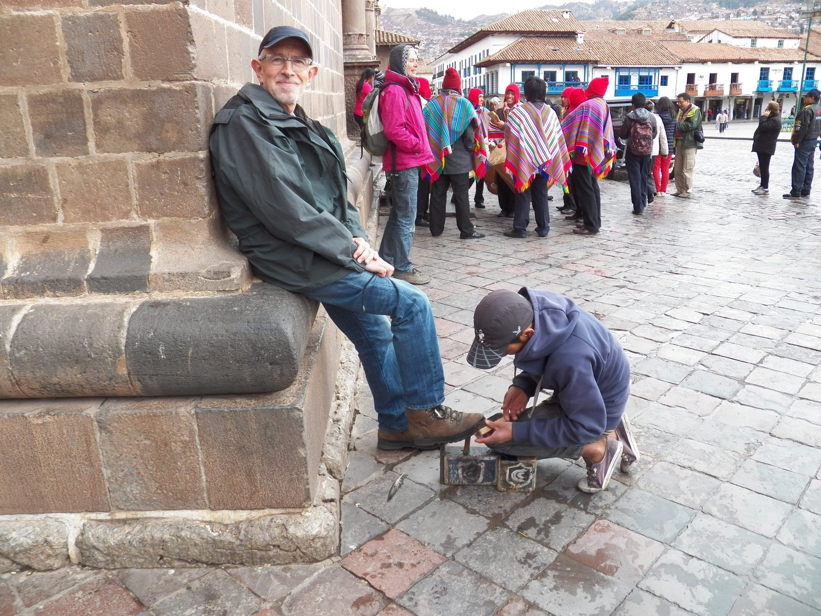 Toerist met schoenpoetser en mensen in poncho's op achtergrond.