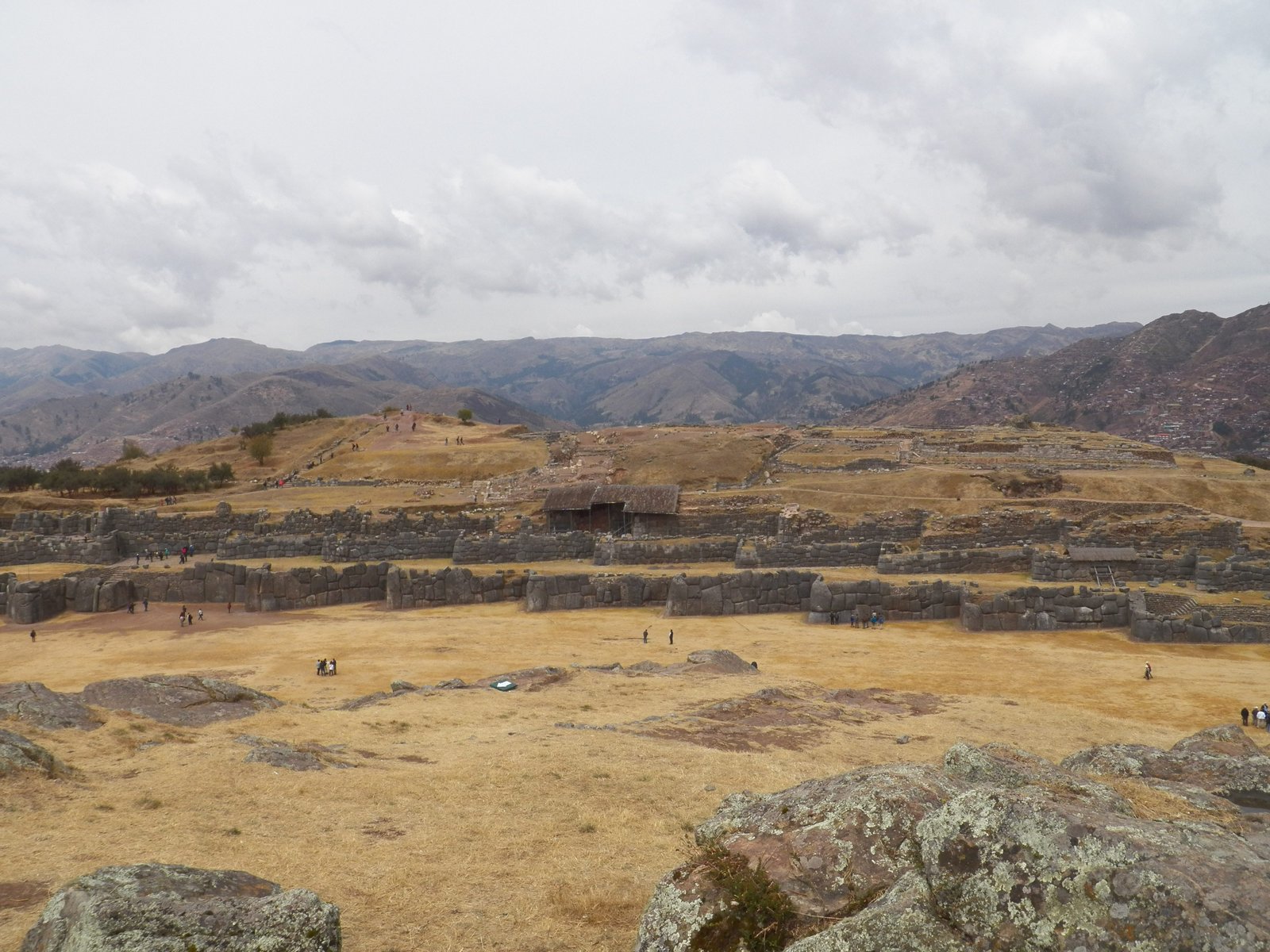 Zicht op muren van Sacsayhuaman op geel grasveld.