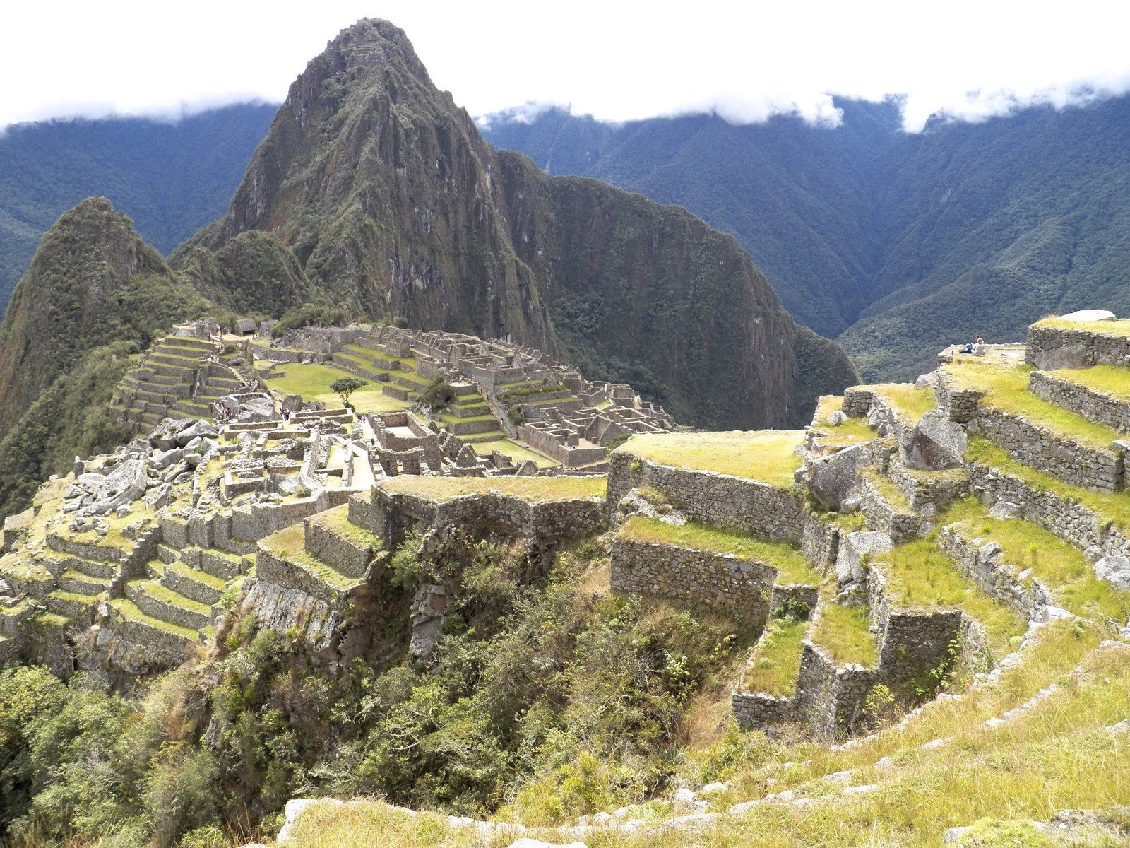 Iconische foto van Machu Picchu in volle zon met witte wolken.