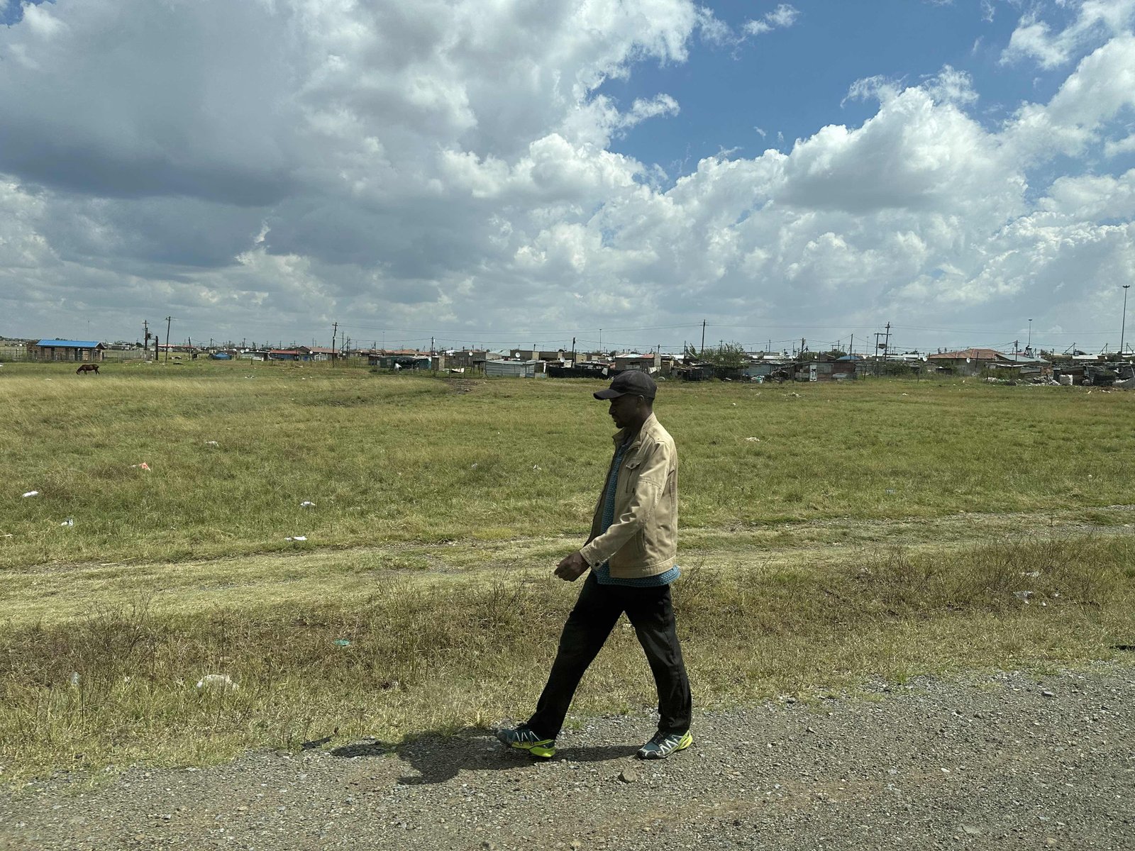 Sasolburg: eenzame man voor grasveld met armoedige wijk op achtergrond. 