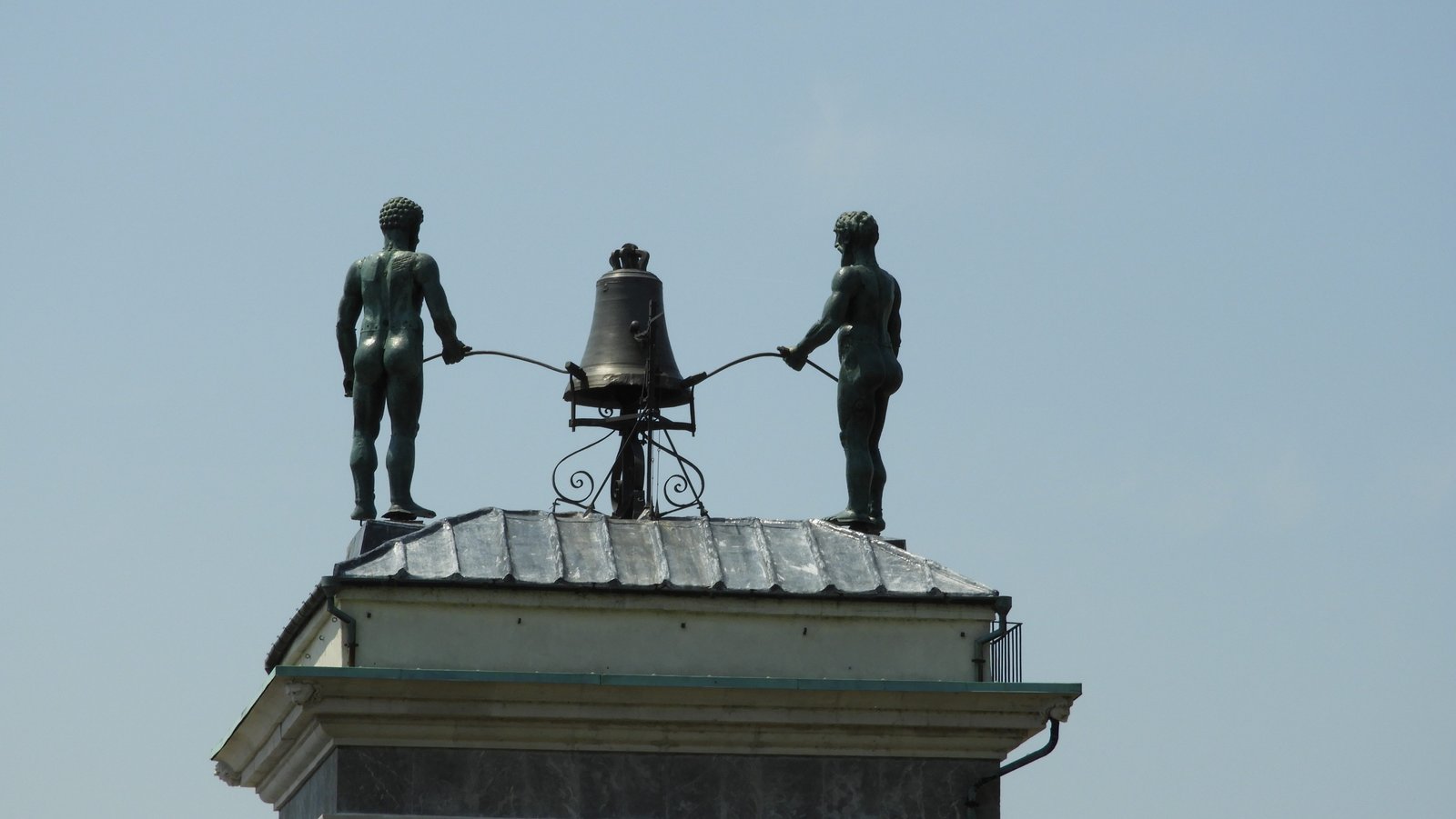 Twee beelden van naakte mannen slaan op klok bovenop klokkentoren.