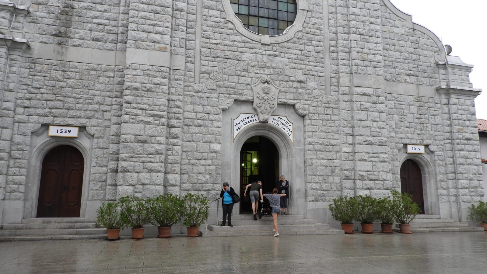 Grijze façade van kerk met drie smalle boogingangen.
