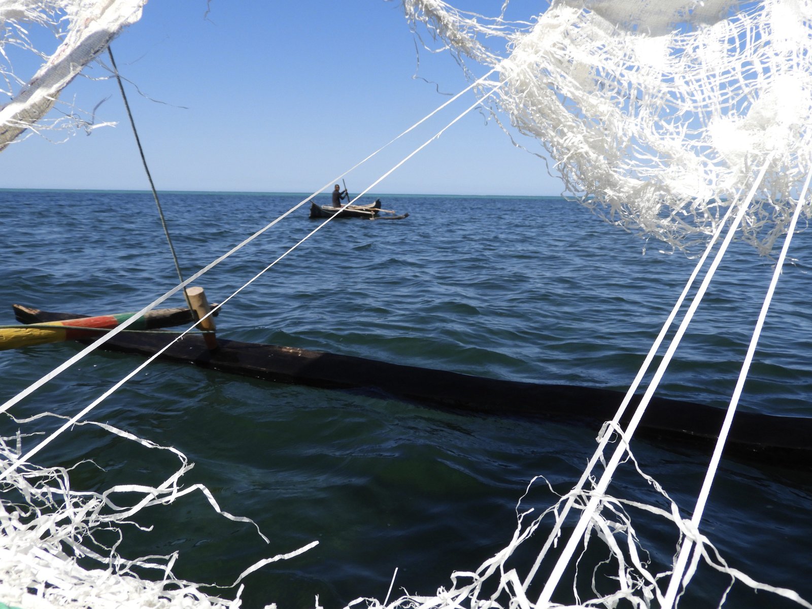 Zee met pirogue doorheen gescheurd zeil van andere boot gefotografeerd.