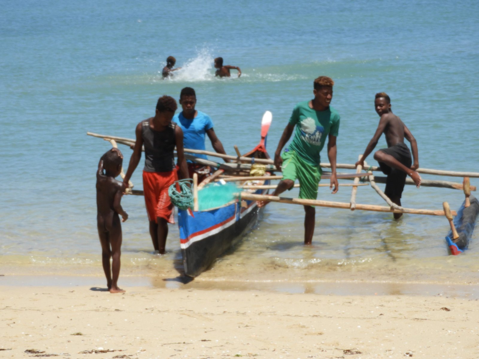 Vissers met blauwe of groene T-shirt trekken pirogue op strand.