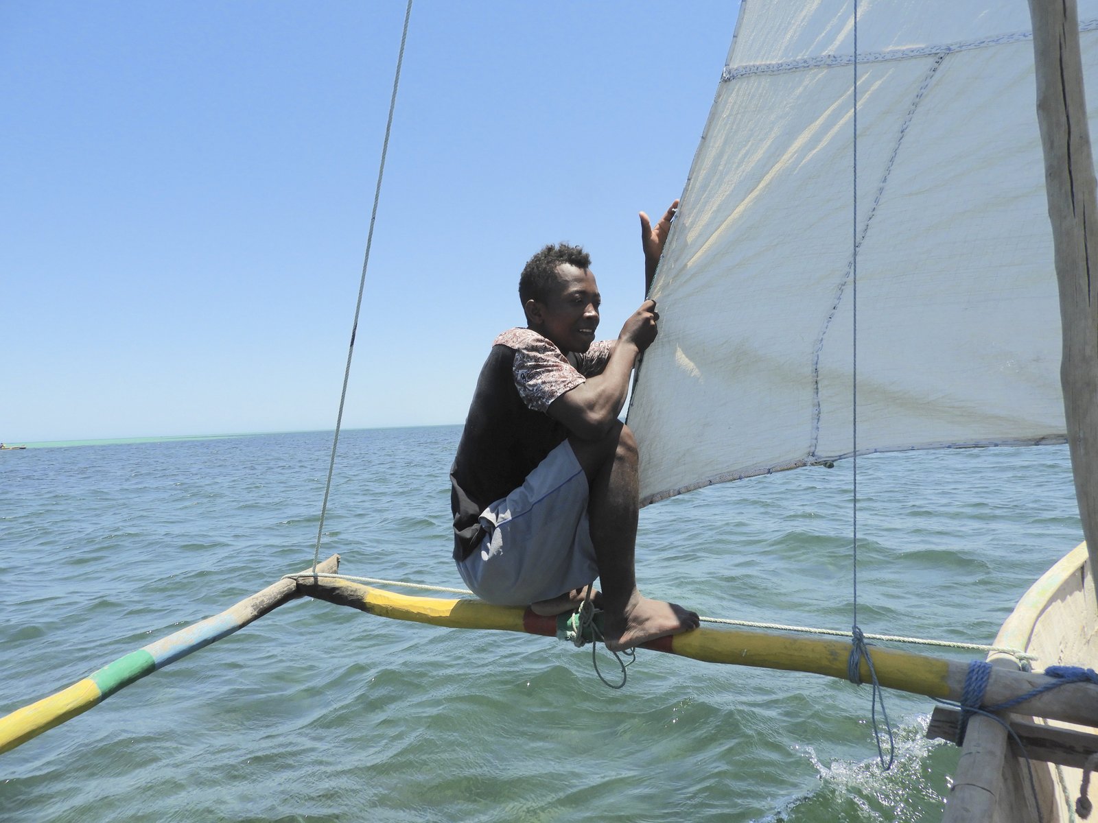 Bootsman zit in pirogue bovenop smal dwarshout boven zee.