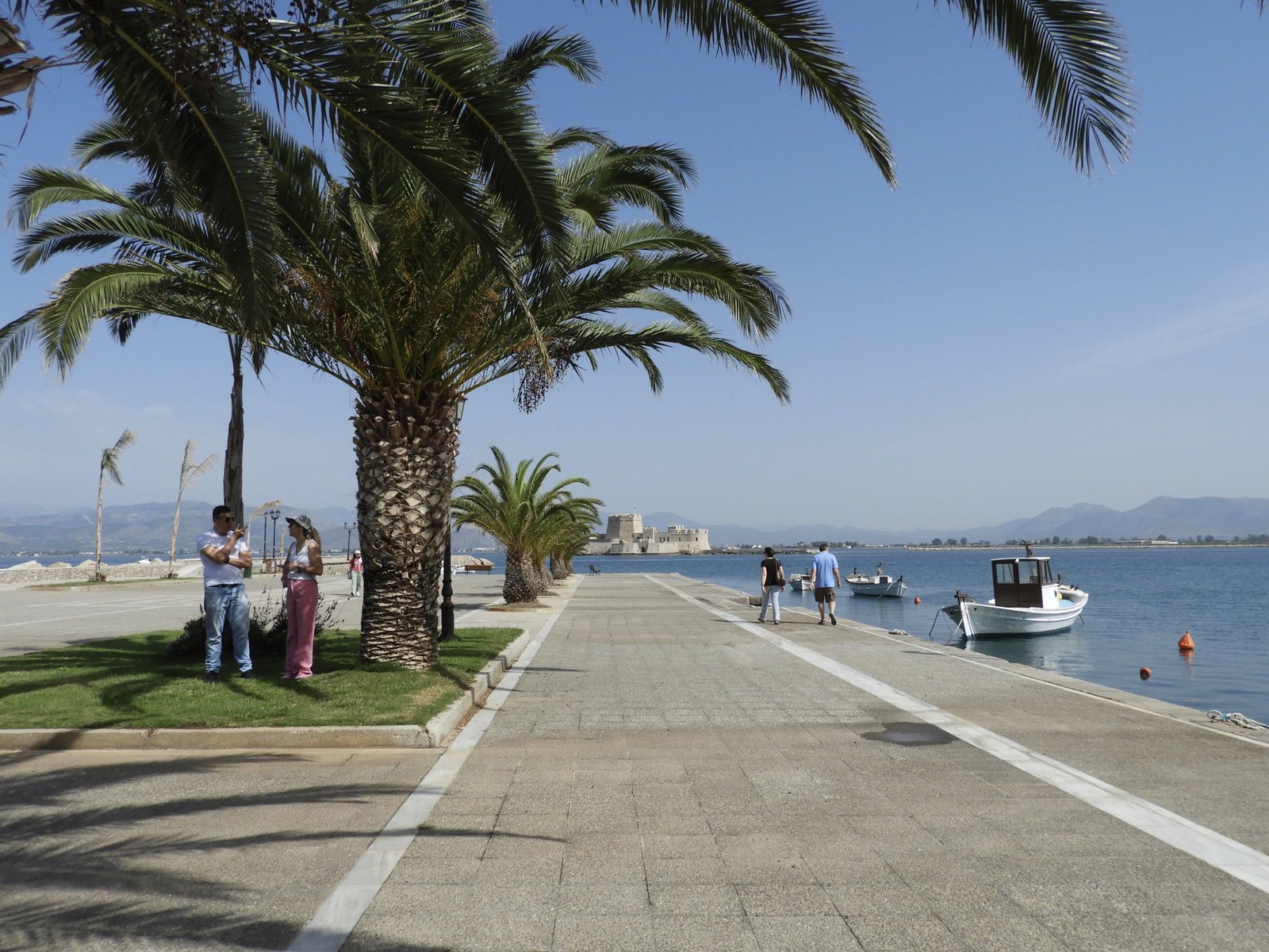 Strandboulevard met palmbomen links, de zee rechts en in het midden Bourtzi, wit kasteeltje.