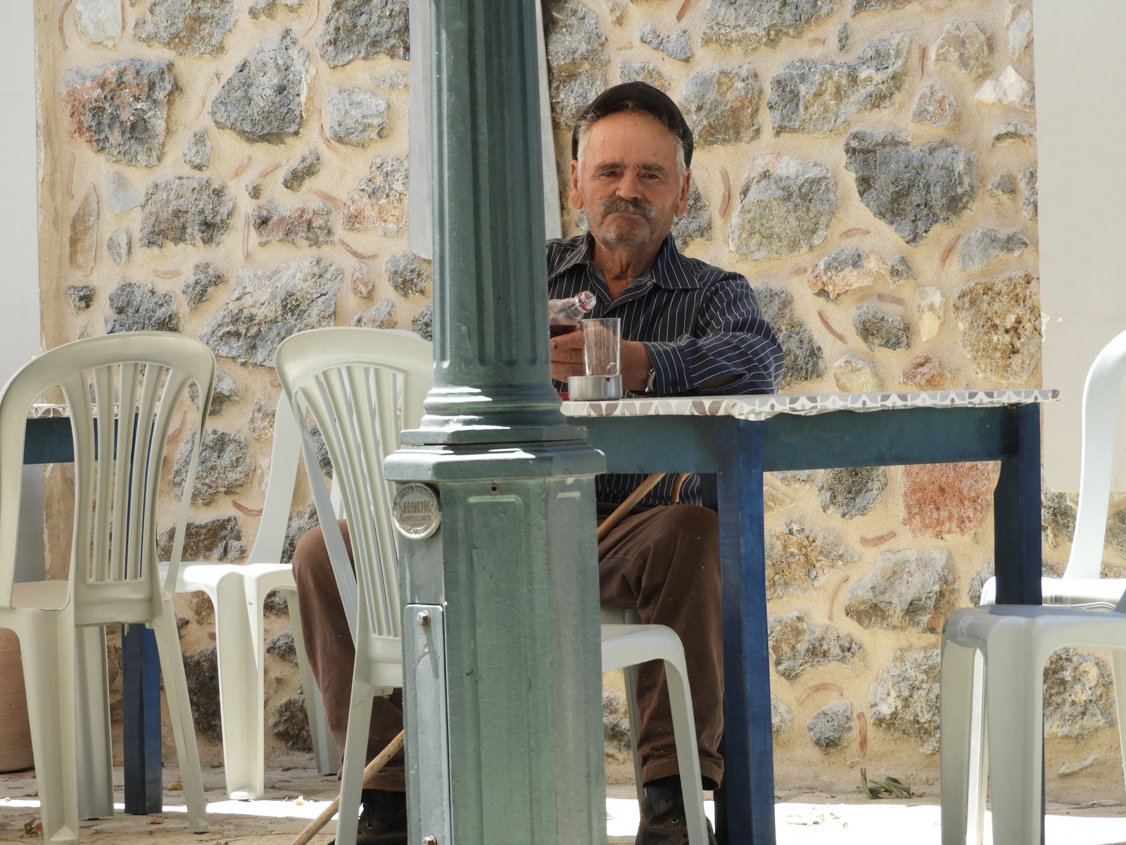 Man met pet en grote snor op terras.