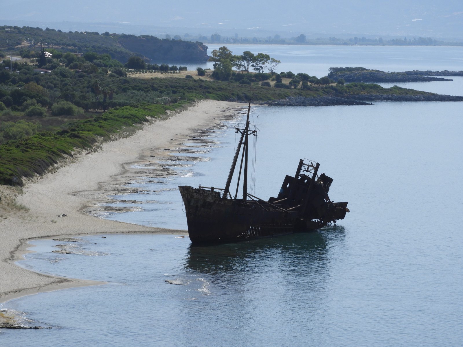 Scheepswrak op het strand met landengte en eilandje op de achtergrond.