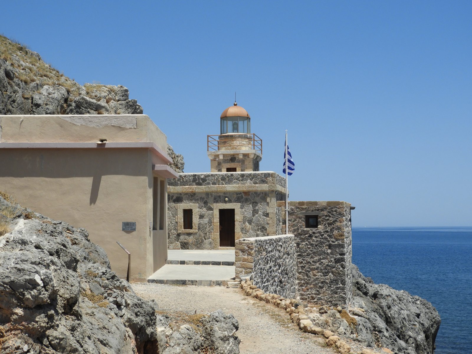 Klein vuurtorentje met Griekse vlag tegen de rotsen op het uiteinde van Monemvasia.