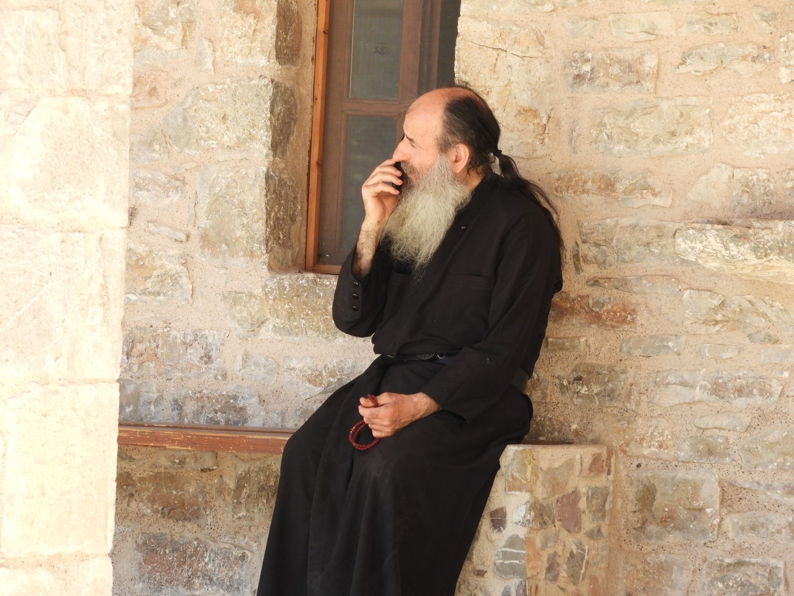 Grieks-Orthodoxe priester in zwarte soutane met smartphone.
