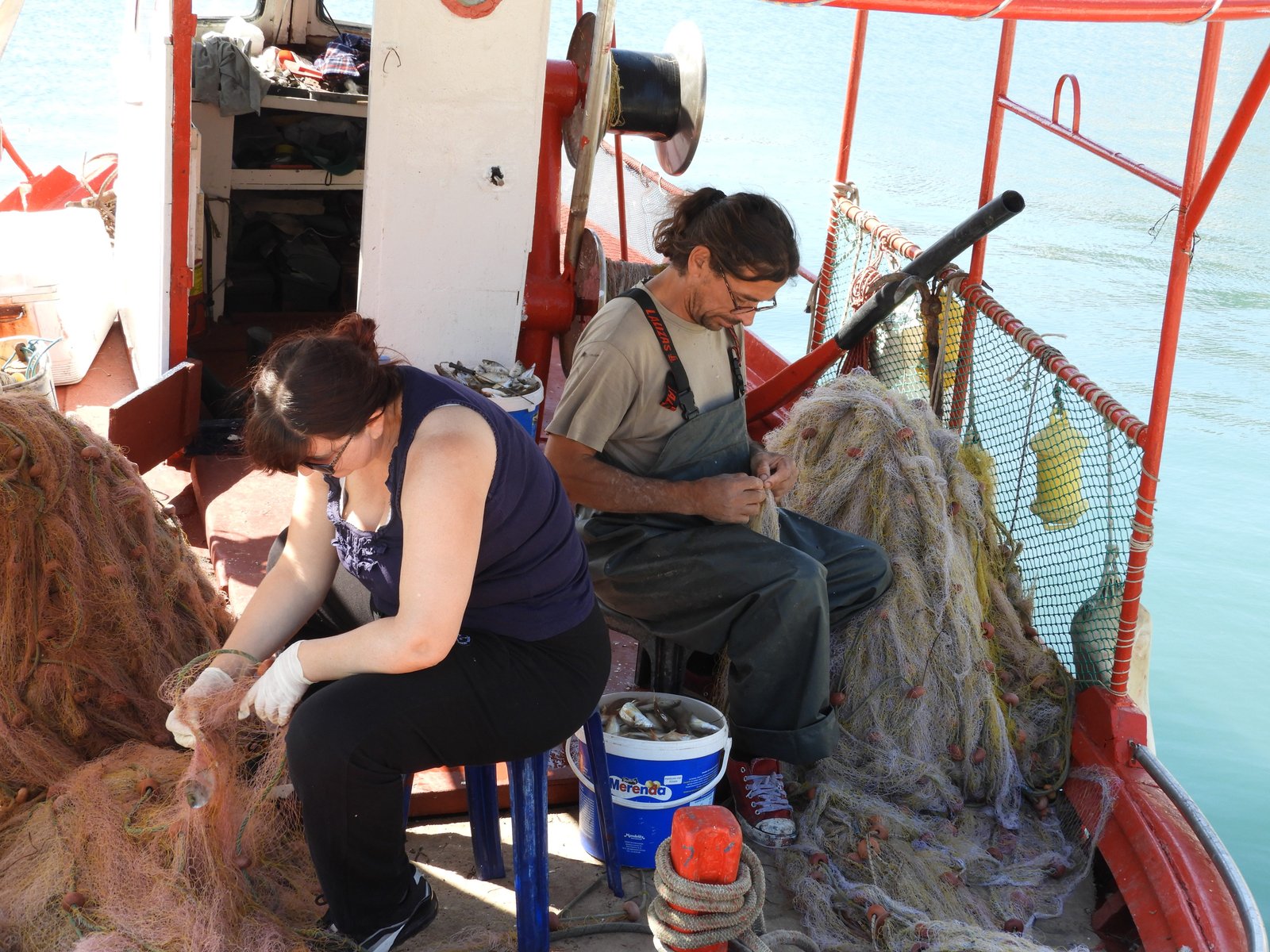 Visser en vrouw herstellen netten op hun boot.