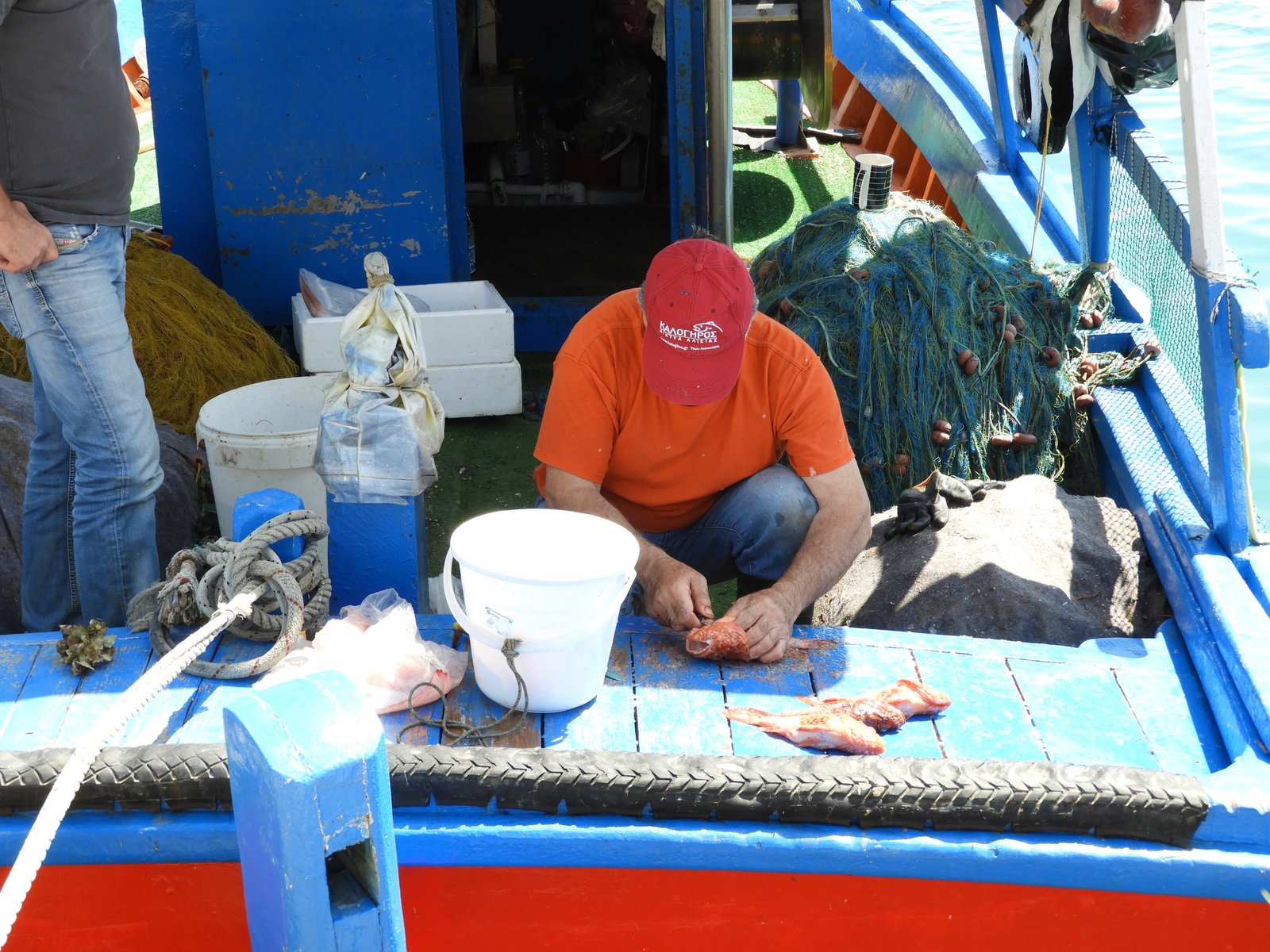Visser in rode T-shirt kuist vis op zijn bootje.