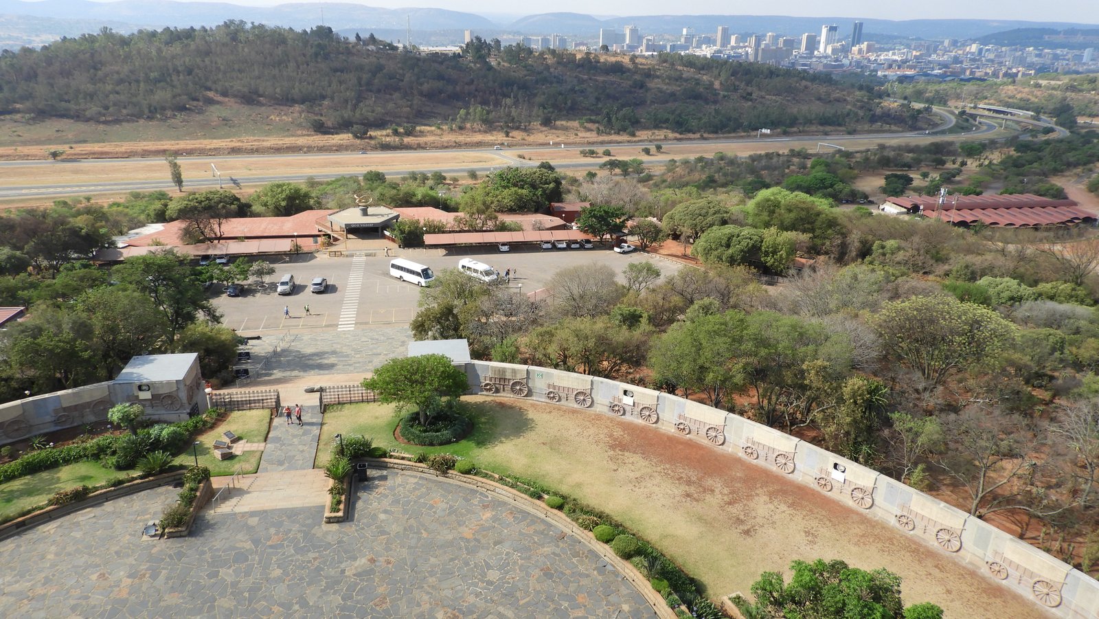 Zicht op cirkel met huifkarren in muur gebeeldhouwd rond het Voortrekkersmonument; Pretoria op de achtergrond.