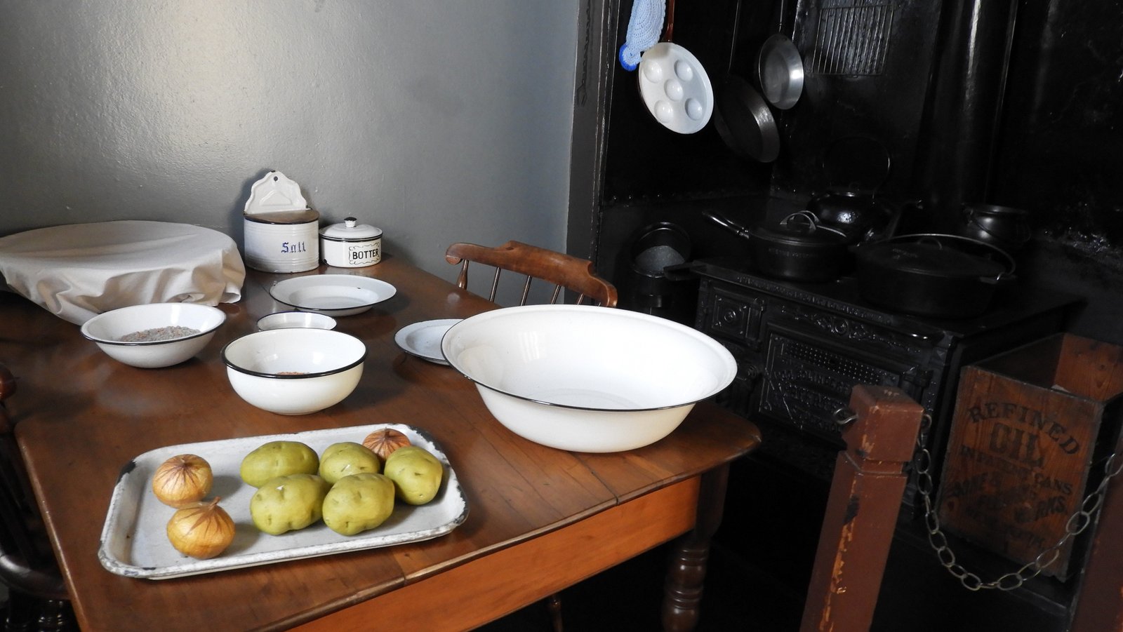 Oude keukentafel met aardappelen en ajuinen in witte schaal en nog witte lege schalen.