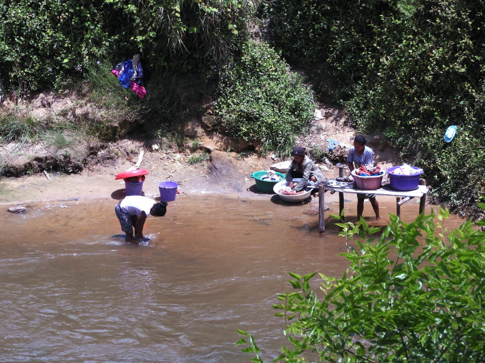 Drie vrouwen doen de was aan de rand van een rivier.