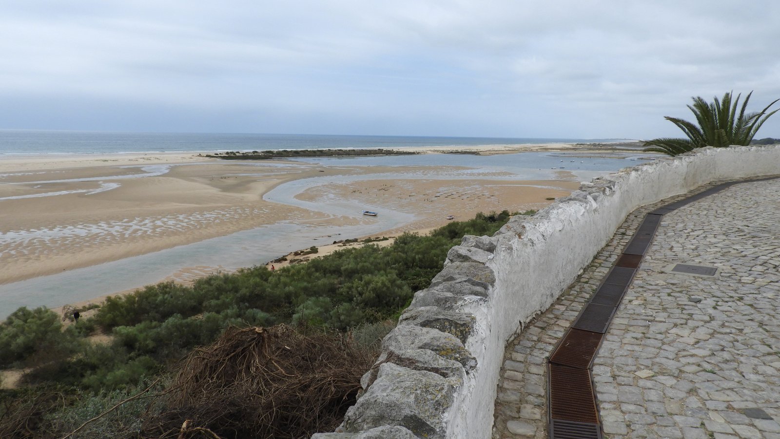 Korte wandelboulevard met links uitgestrekt strand, zee en meanderende riviertjes.