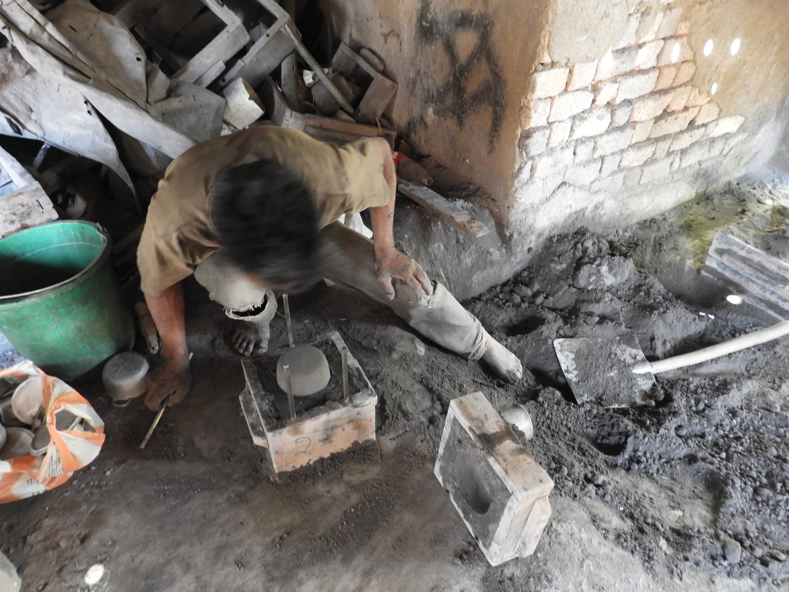 Man damt mengel van houtskool en zand aan om aluminium pot te maken.