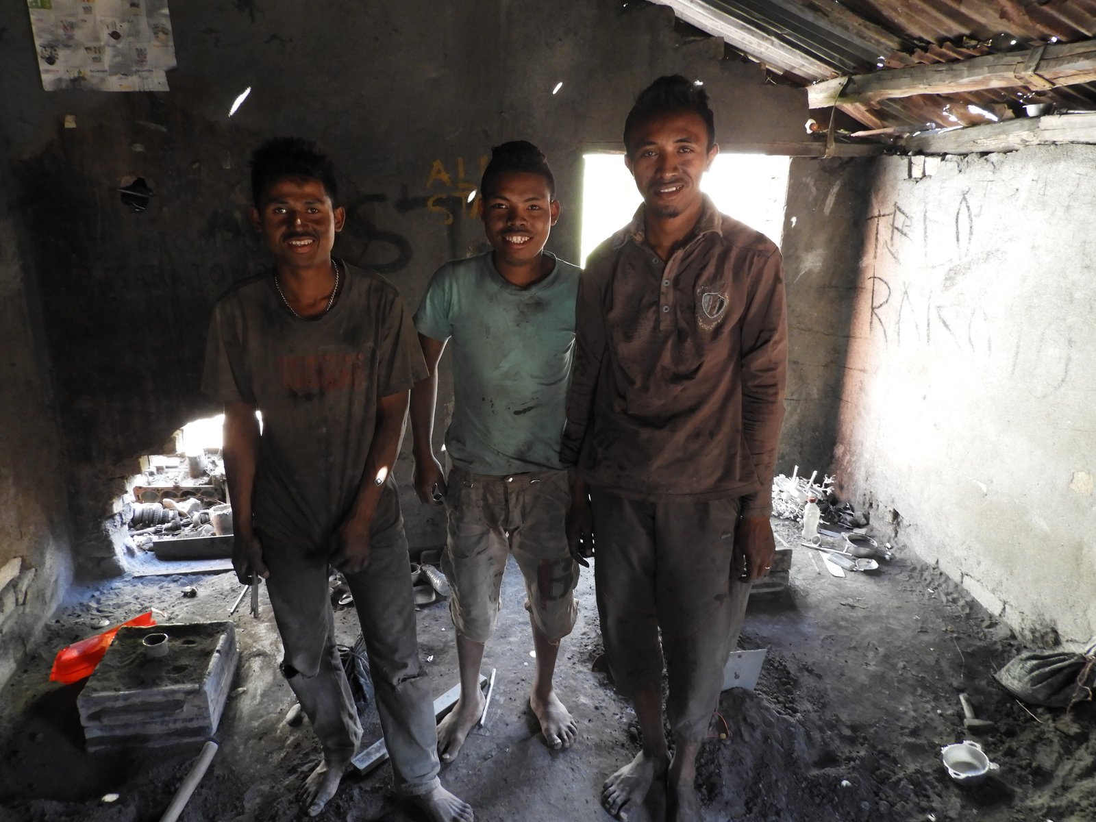 Drie jongens in vuile kleedje op blote voeten in aluminium-fabriekje.