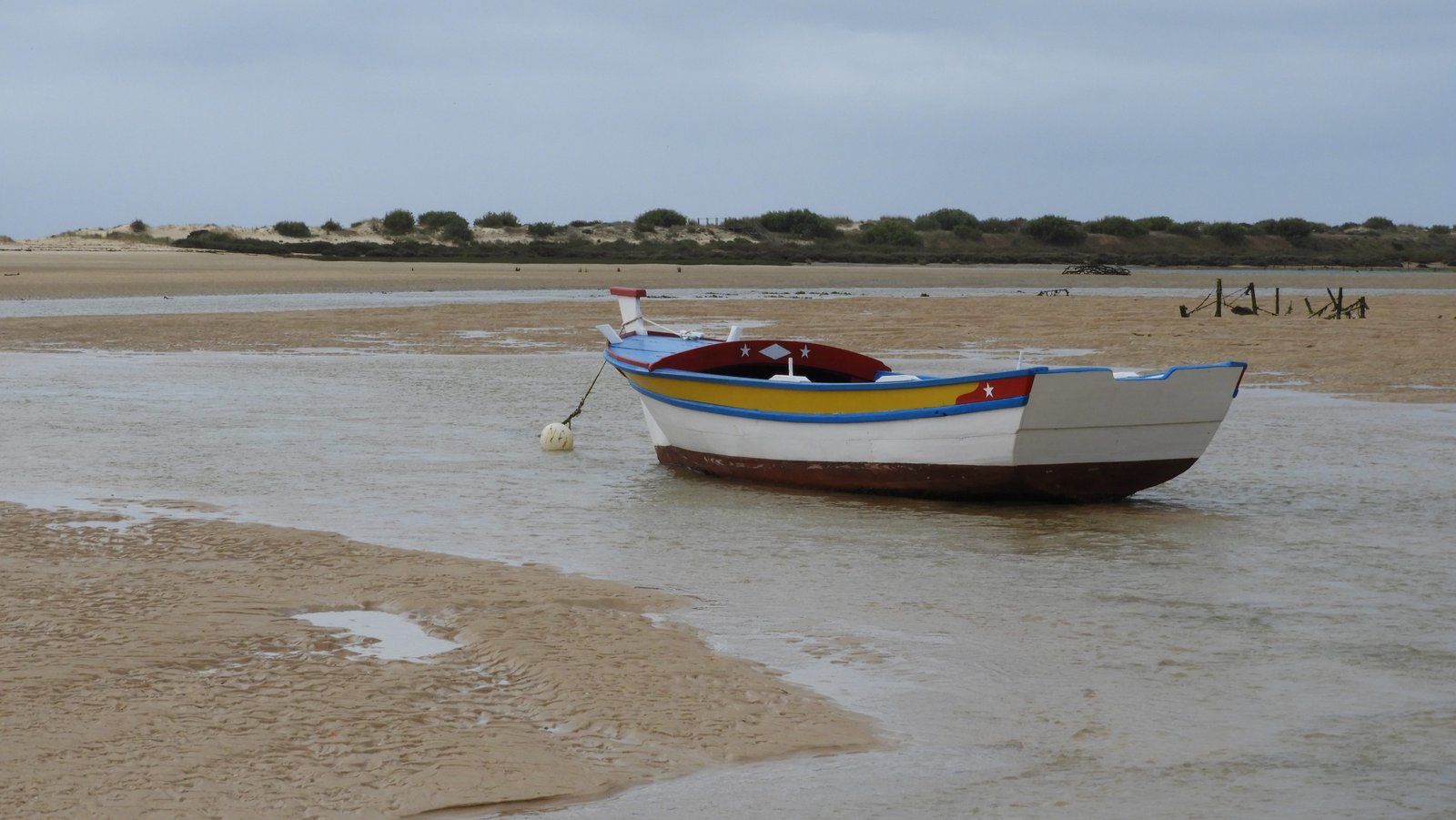 Roeibootje met blauwe, geel, rood en wit als kleuren op strand.