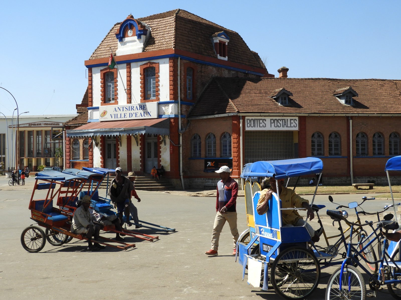 Verschillende blauwe pousse-pousse voor koloniaal gebouw in Antsirabe.