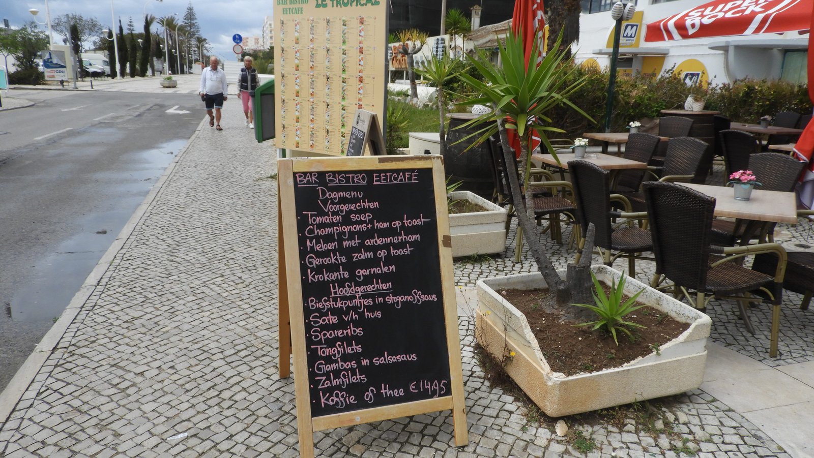 Bord met menu in het Nederlands tussen voetpad en terras.