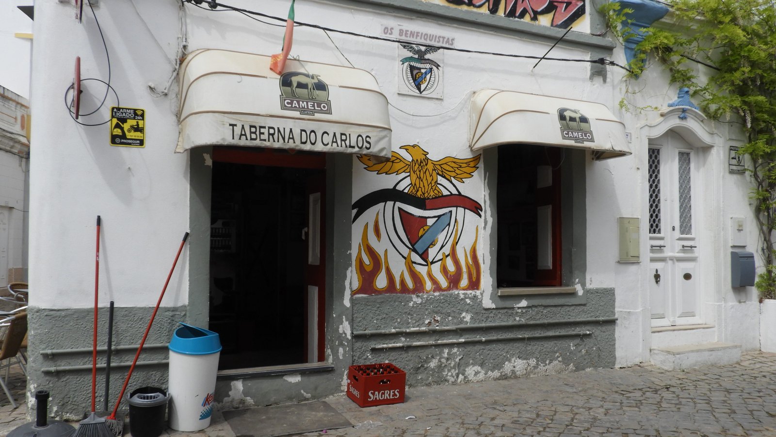 Taberna do Carlos: klein cafeetje in wit met kleurrijk embleem van voetbalploeg Benfica.