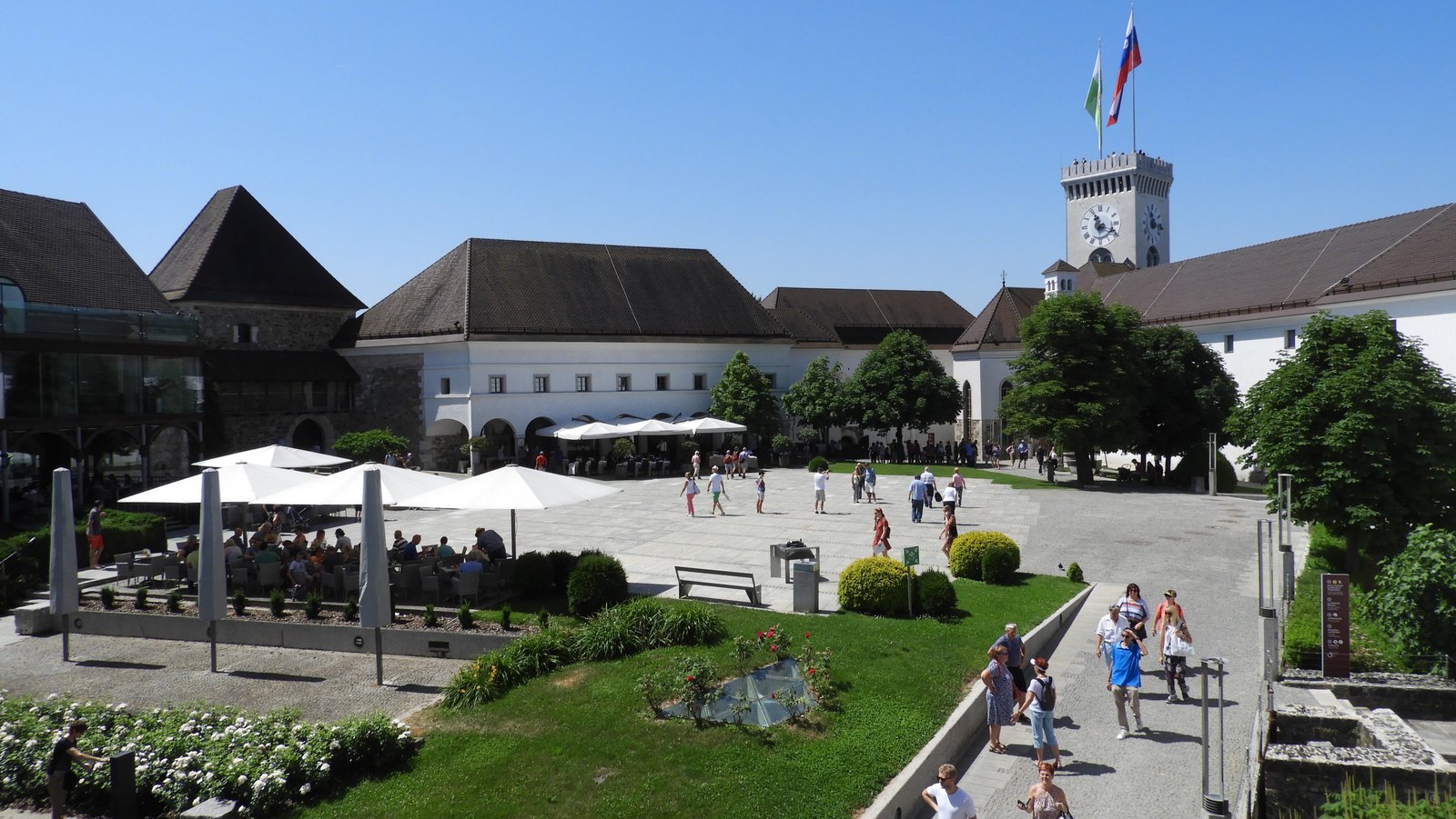 Binnenplein van kasteel met terras onder witte parasol en witte gebouwen met grijze daken rondom.