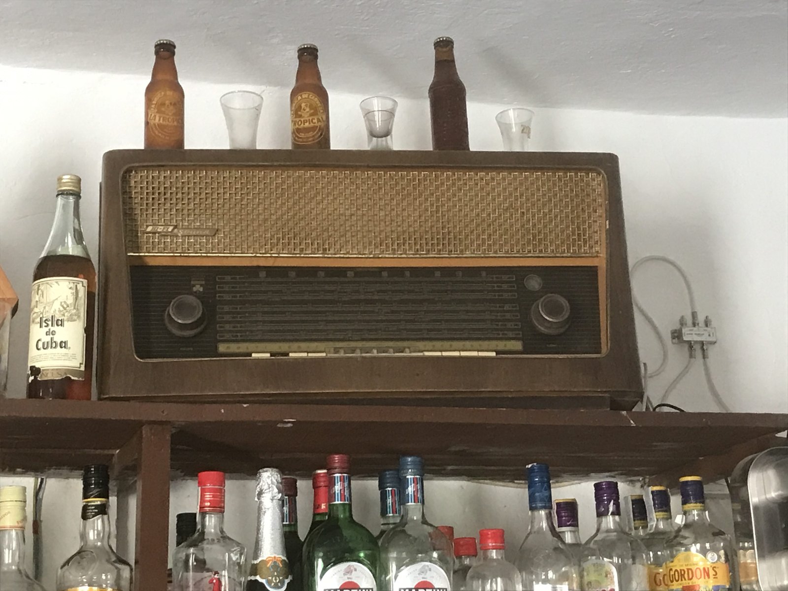 Grote antieke radio boven schap met drankflessen.