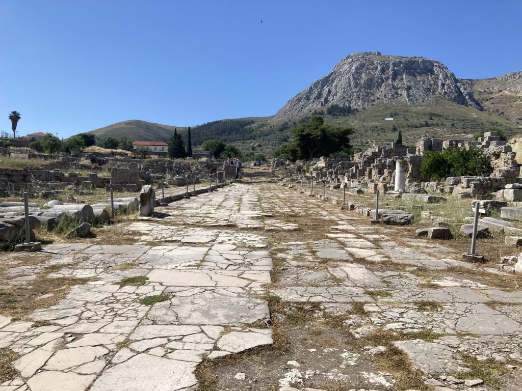 Ruïne van geplaveide straat in Korinthe met berg van Acrocorinth op achtergrond.