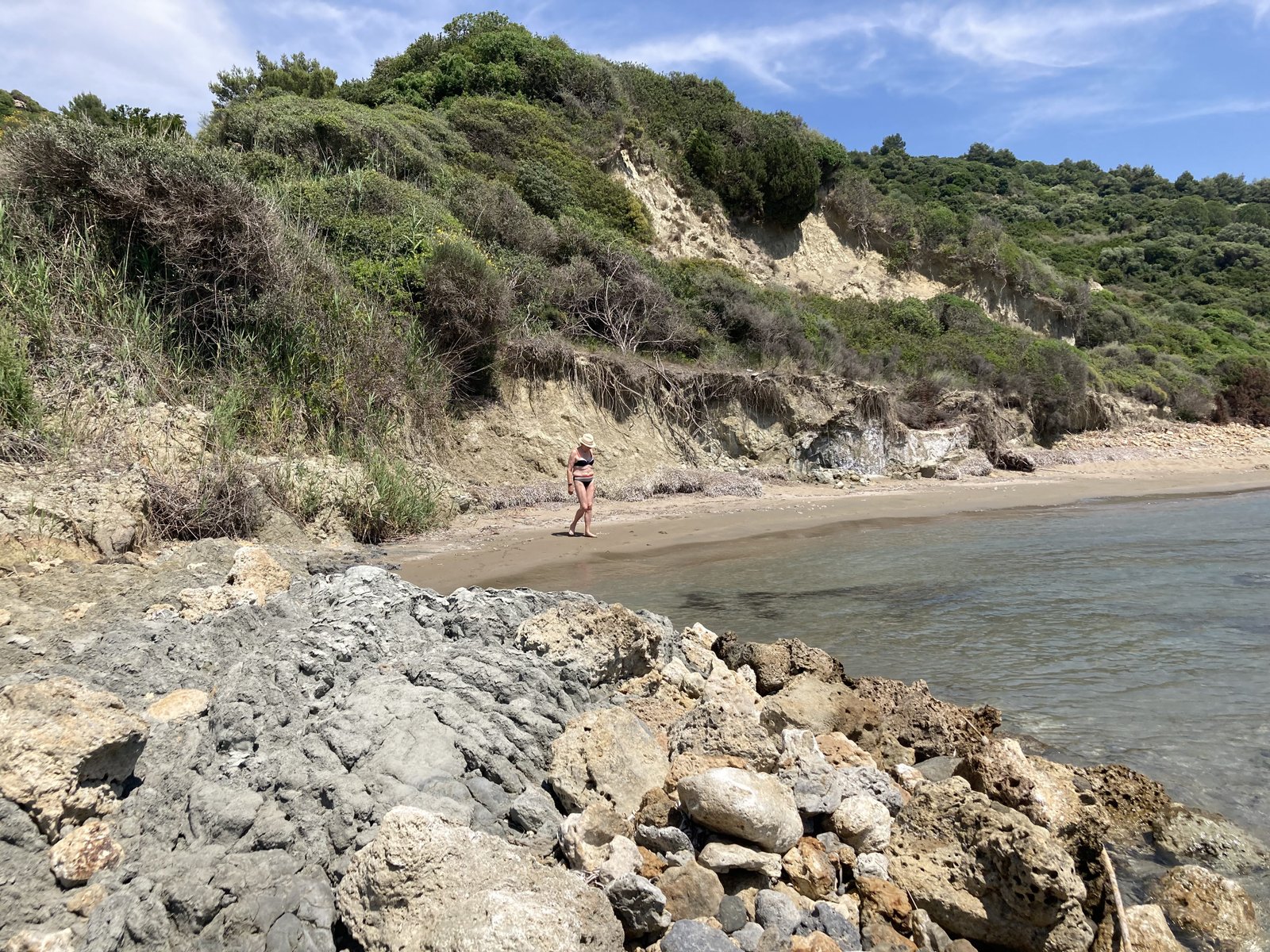 Baai met rotsen, strand, toeriste en heuvel.