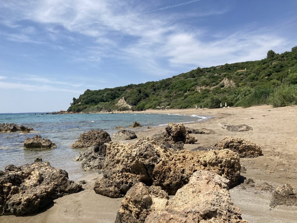 Baai met rotsen, strand en groene heuvels.