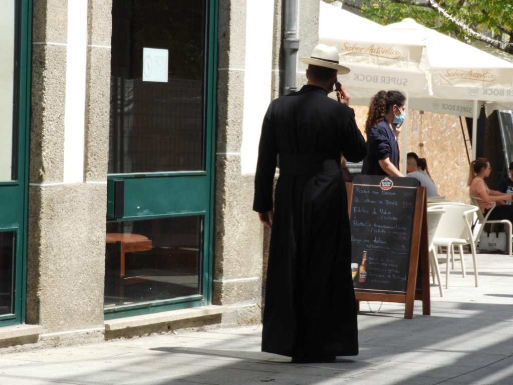 Pastoor in zwart habijt met smartphone. 