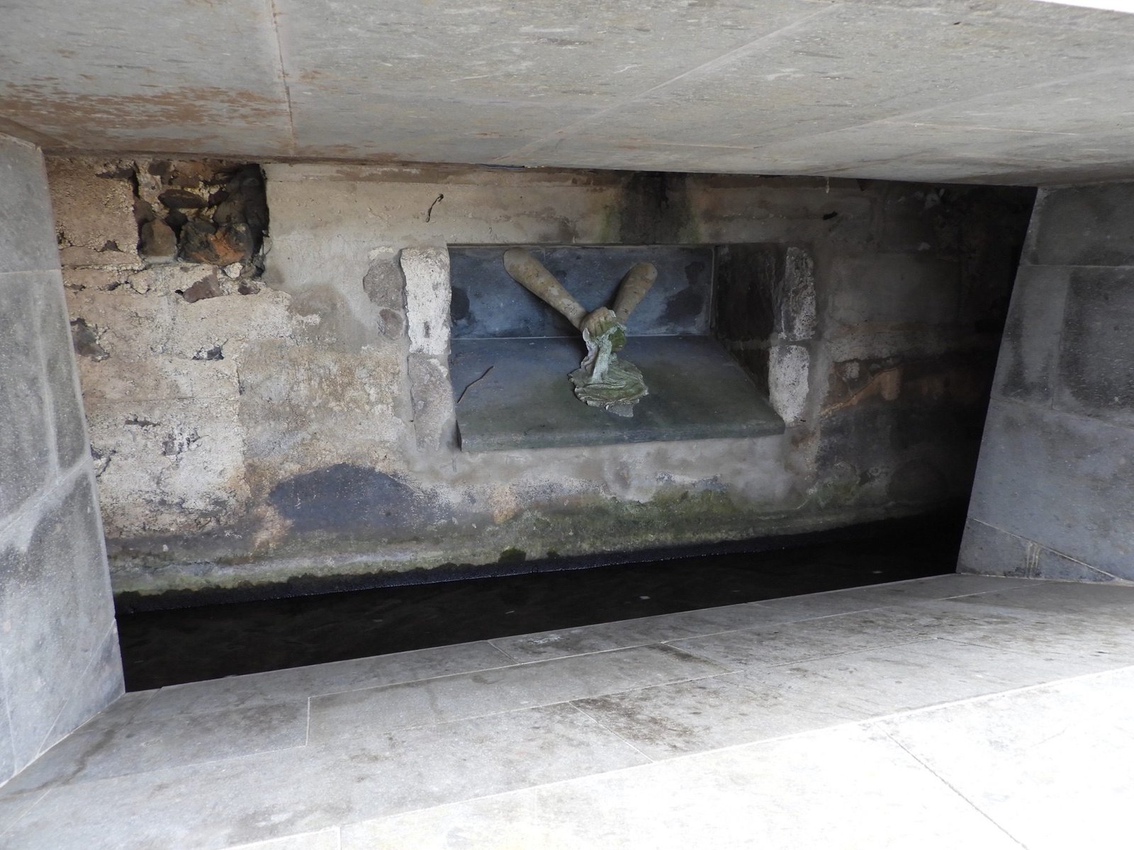 Ondergronds waterkanaal met gebeeldhouwde handen in muur.