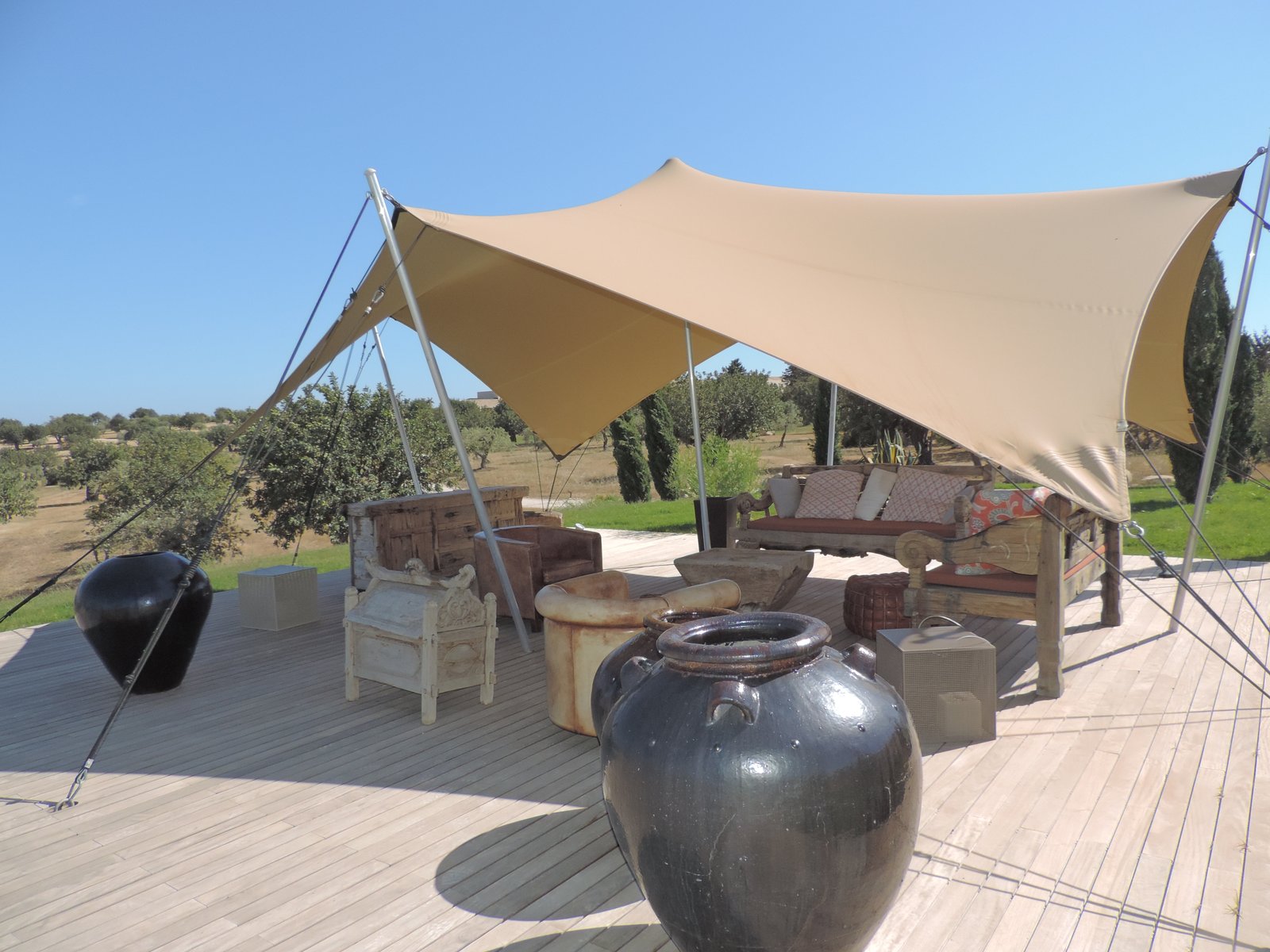 Houten terras met grote kruiken onder beige zeildoek.