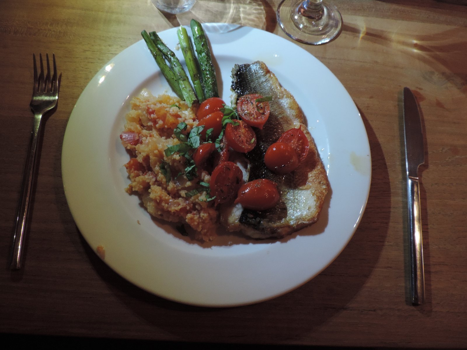 Bord met zeebaars, groene asperges, couscous en tomaatjes.