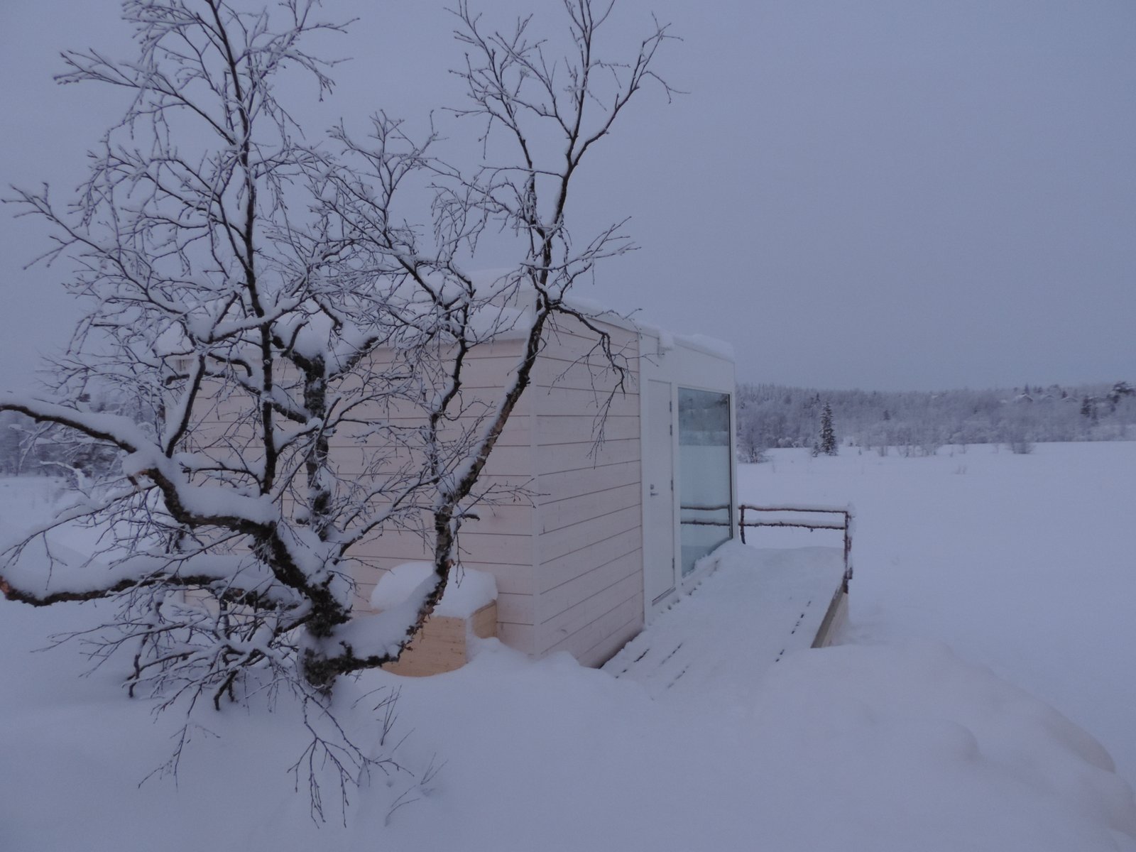 Klein houten chalet met veel glas in sneeuwlandschap.