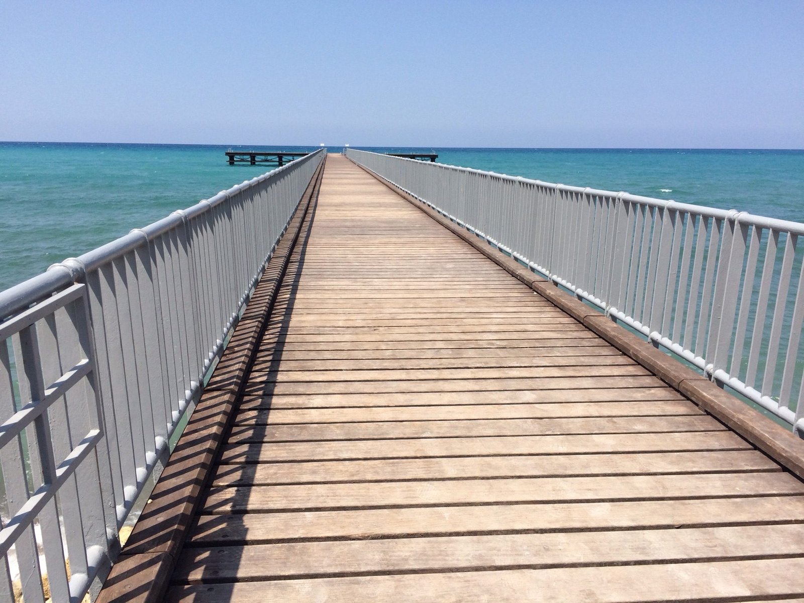 Eondeloos lijkende pier in blauwe zee.