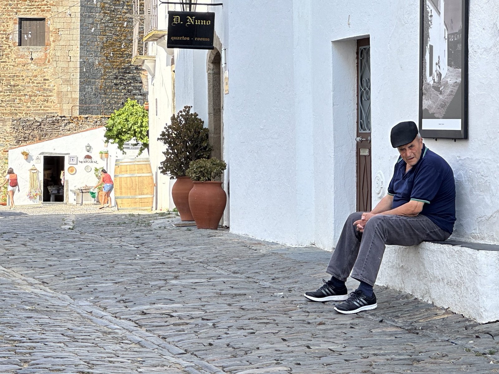 Oude Portugees op stenen bankje voor wit huis in Monsaraz, Alentejo