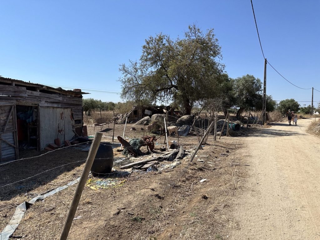 Grindweg naar Menhir do Outeiro, Alentejo met krotwoning, veel rommel en geit