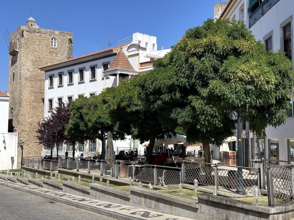 Pleintje met oude vierkante toren, veel schaduw van bomen en terras in Elvas