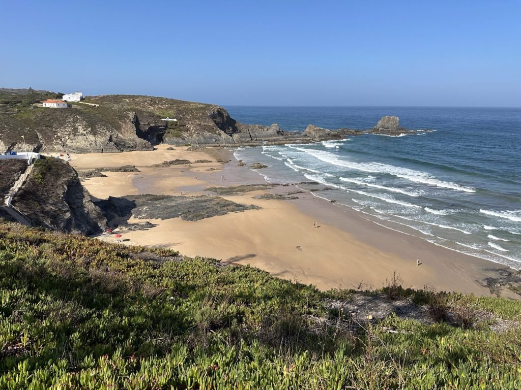 Baai met strand, blauw water, groene begroeiing in Zambujeira
