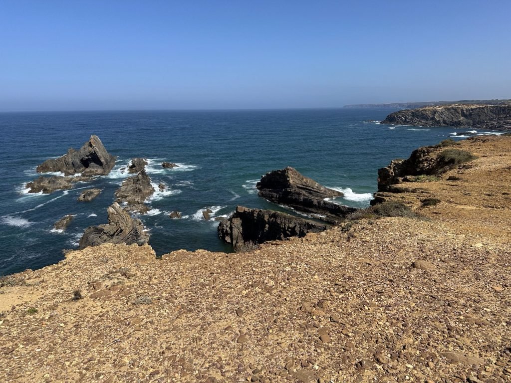Rotsen en droge begroeiing op voorgrond, zee met rotsen op achtergrond op de Rota Vicentina, Zambujeira.