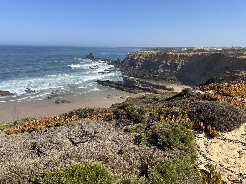 Baai met rotsen en blauwe zee, op voorgrond: typische mediterrane begroeiing op de Rota Vicentina