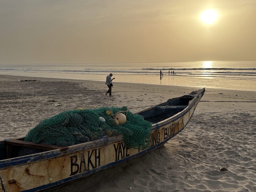Oude pirogue op het strand, enkele mensen, zonsondergang 