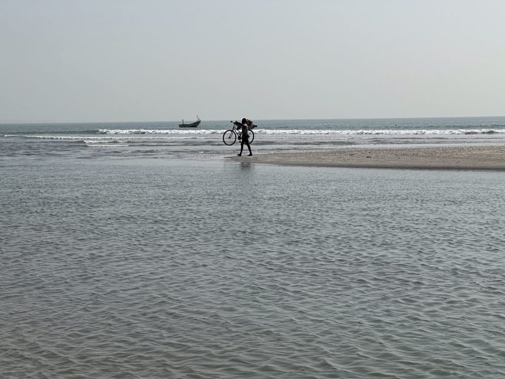 Fietser met fiets op schouder op zandbank in de zee