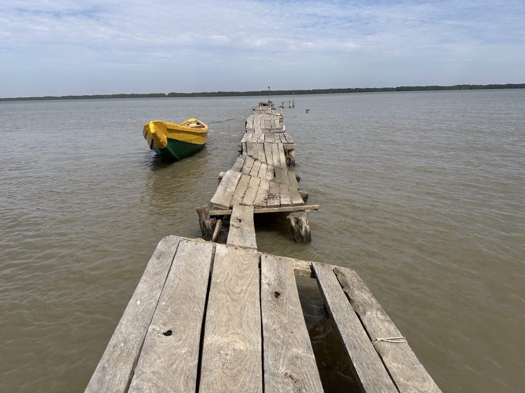 Gammele houten steiger in de Gambia-rivier met geel bootje