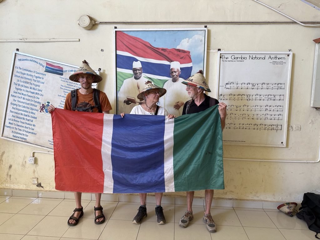 Drie toeristen met strohoeden houden de vlag van Gambia vast. 