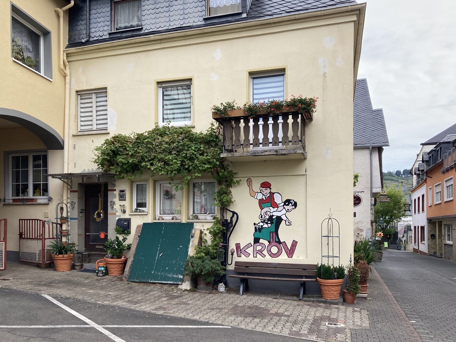 Licht-beige huis met muurschildering van wijnboer die kind billenkoek geeft.